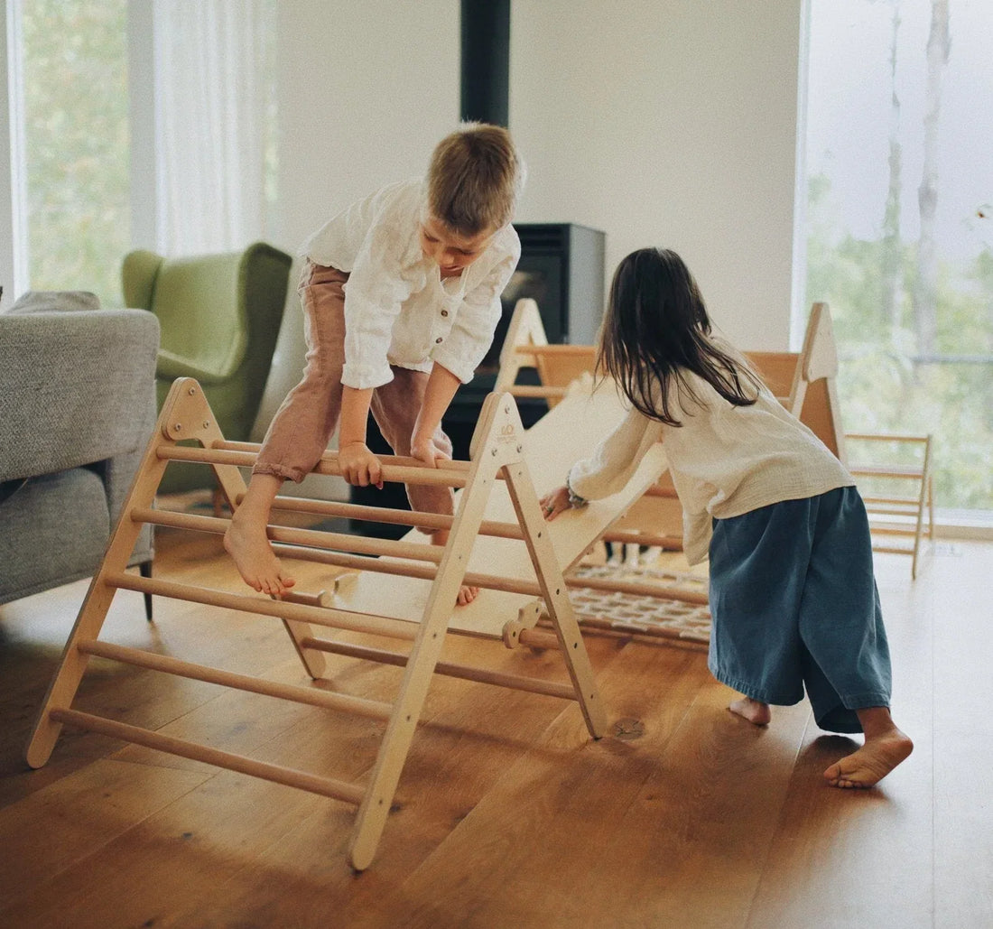 Two children playing and climbing on a Kinderfeets Pikler Triangle in a bright, modern living room
